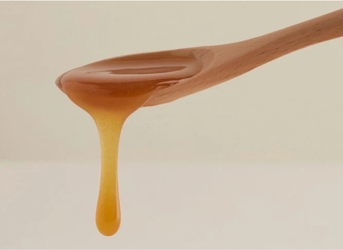 Miele denso ambrato scuro che cola da un cucchiaino di legno